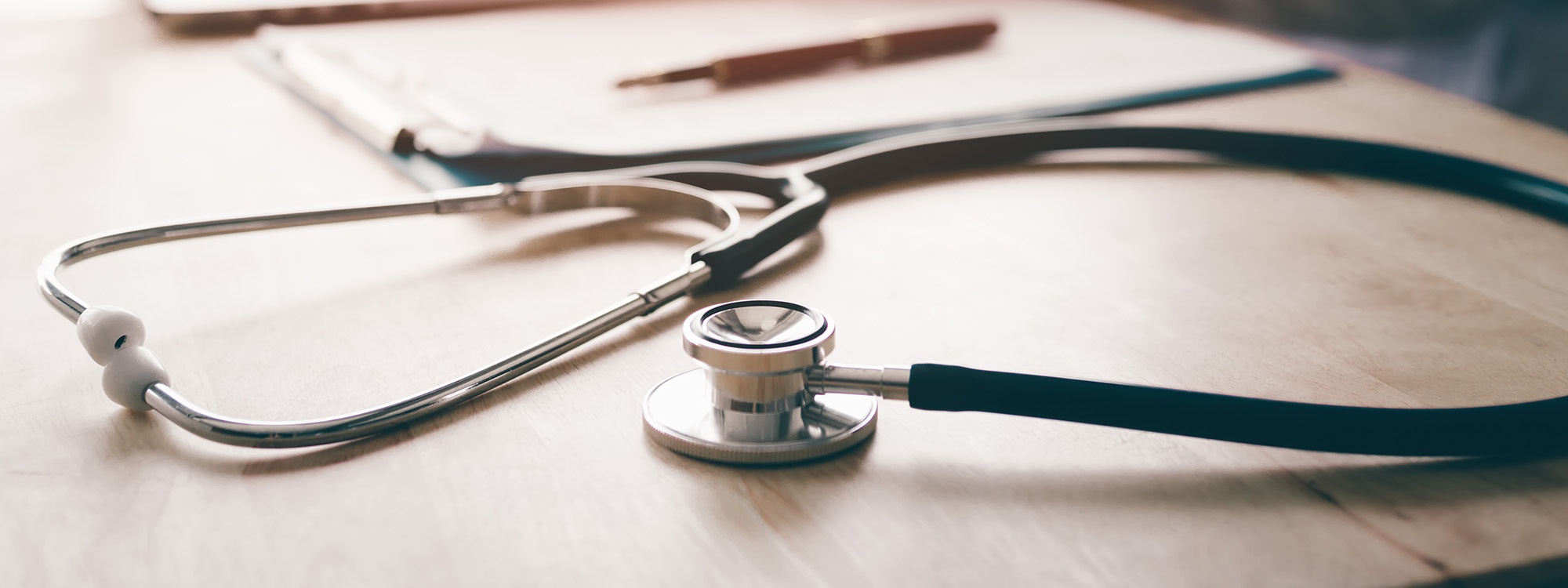 Stethoscope and background doctor using laptop at desk in clinic